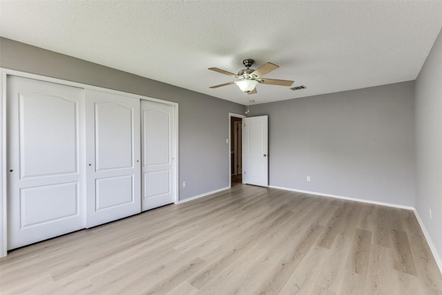 unfurnished bedroom featuring a closet, light wood-type flooring, baseboards, a textured ceiling, and a ceiling fan