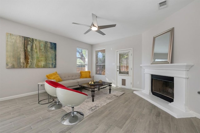 living area featuring wood finished floors, a ceiling fan, a fireplace with raised hearth, and baseboards