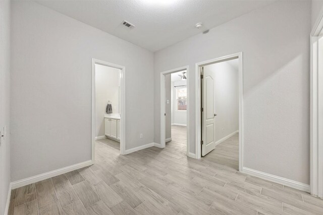 unfurnished bedroom with light wood-style flooring, baseboards, and connected bathroom