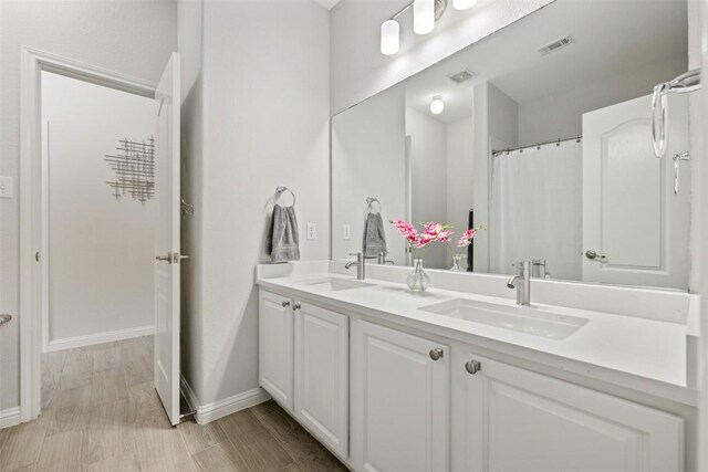 full bathroom featuring baseboards, double vanity, and wood finished floors