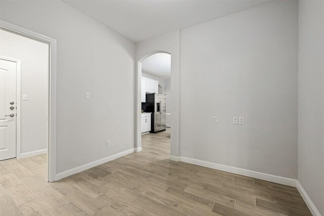 empty room featuring arched walkways, light wood-type flooring, and baseboards