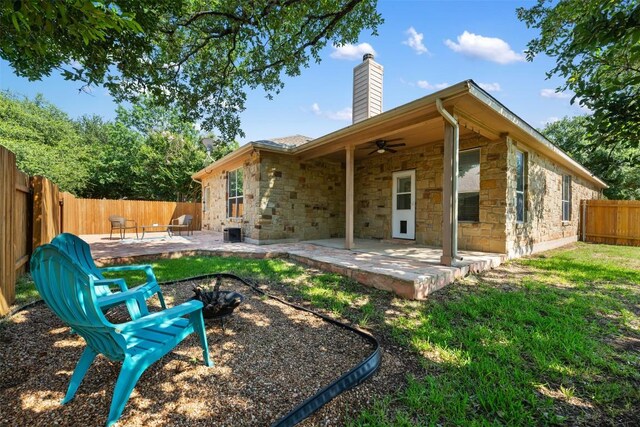 rear view of property with ceiling fan, a chimney, a patio area, a fenced backyard, and stone siding