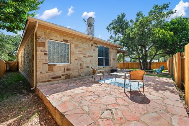 back of house with stone siding, a patio area, a fenced backyard, and a chimney