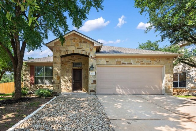 view of front of property with stone siding, a garage, driveway, and fence