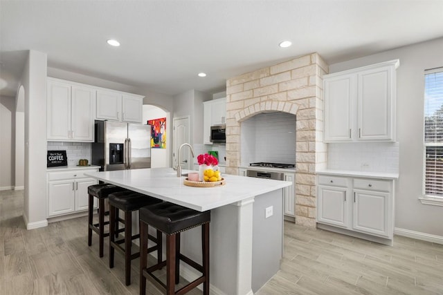 kitchen with stainless steel appliances, decorative backsplash, arched walkways, light wood finished floors, and recessed lighting