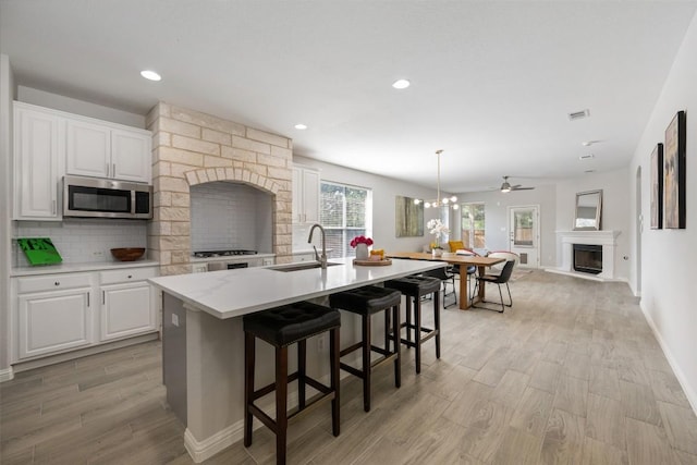 kitchen featuring a fireplace, stainless steel microwave, a sink, light wood finished floors, and light countertops