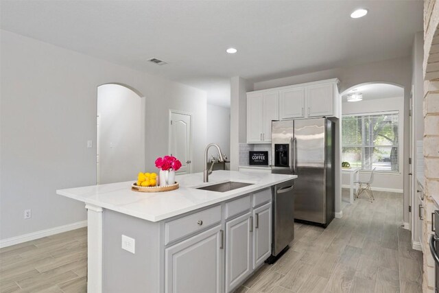 kitchen featuring appliances with stainless steel finishes, a sink, arched walkways, baseboards, and light countertops