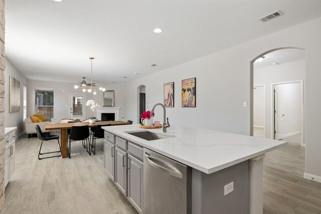 kitchen featuring stainless steel dishwasher, a sink, gray cabinetry, open floor plan, and a fireplace