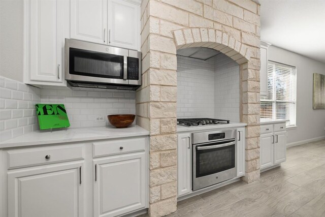 kitchen featuring appliances with stainless steel finishes, backsplash, white cabinetry, light countertops, and light wood-style floors