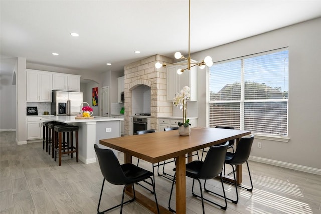 dining space featuring arched walkways, baseboards, a chandelier, light wood-type flooring, and recessed lighting