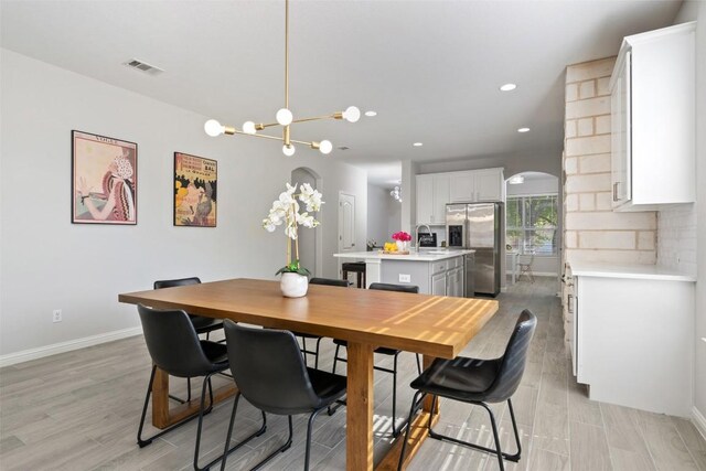 dining area with arched walkways, light wood-type flooring, baseboards, recessed lighting, and a chandelier