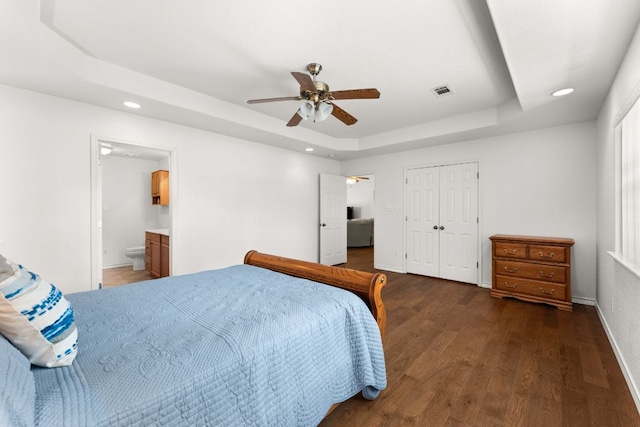 bedroom with a raised ceiling, recessed lighting, wood finished floors, baseboards, and a closet