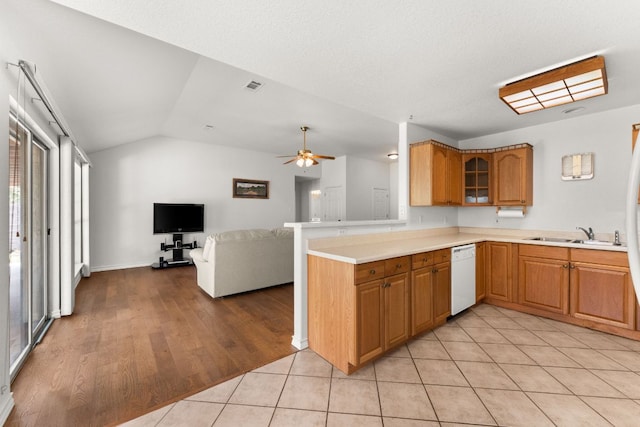 kitchen with white dishwasher, a sink, light countertops, lofted ceiling, and ceiling fan