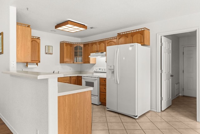 kitchen with white appliances, under cabinet range hood, a peninsula, light countertops, and brown cabinets