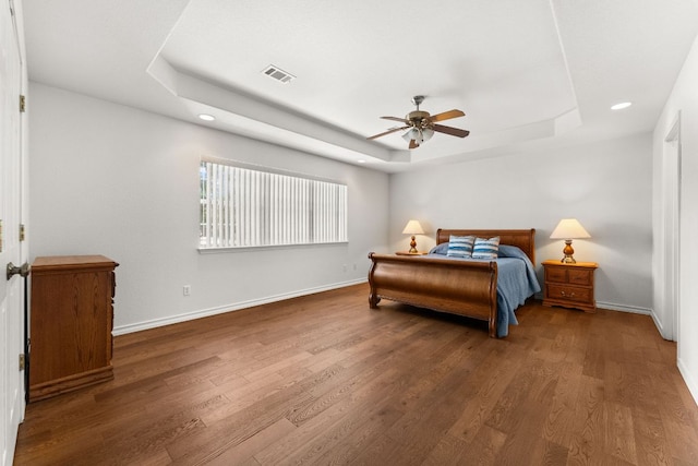bedroom with a tray ceiling, wood finished floors, recessed lighting, baseboards, and ceiling fan
