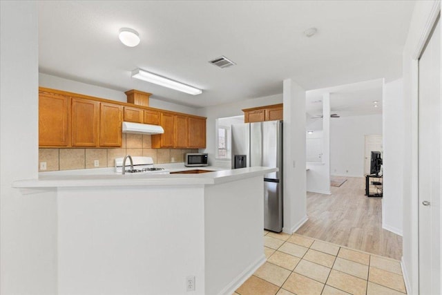 21223 Byerly Turk Dr, Pflugerville, TX 78660 - kitchen featuring under cabinet range hood, stainless steel appliances, light countertops, a peninsula, and tasteful backsplash