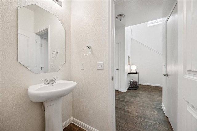 bathroom with wood finished floors, baseboards, a textured wall, and a sink
