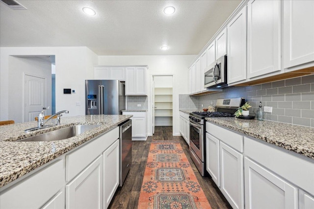 kitchen featuring stainless steel appliances, a sink, dark wood-style floors, white cabinets, and backsplash
