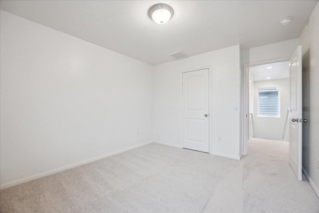 unfurnished bedroom featuring light carpet, baseboards, and a textured ceiling