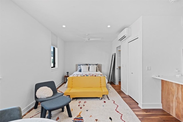 bedroom featuring a wall mounted AC, wood finished floors, baseboards, recessed lighting, and ceiling fan