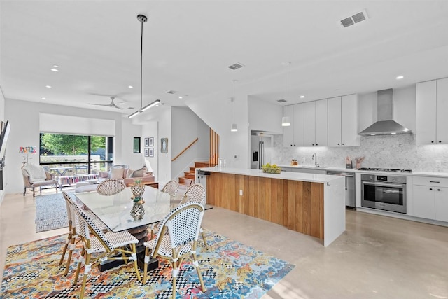 kitchen with appliances with stainless steel finishes, wall chimney exhaust hood, a sink, open floor plan, and decorative backsplash