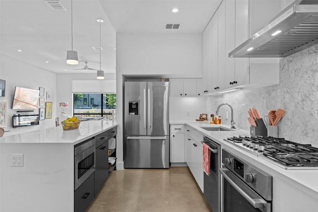 kitchen featuring appliances with stainless steel finishes, wall chimney range hood, a sink, tasteful backsplash, and light countertops