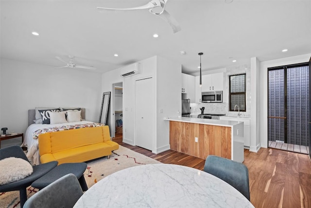 bedroom featuring a wall mounted AC, light wood-type flooring, fridge, recessed lighting, and a sink