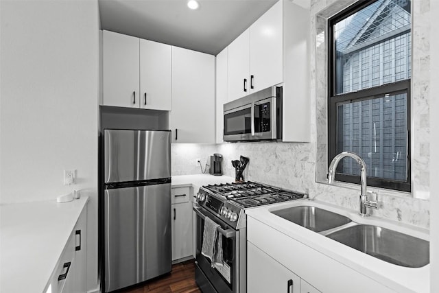 kitchen with appliances with stainless steel finishes, a sink, light countertops, tasteful backsplash, and white cabinets