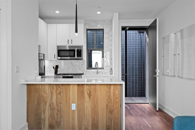 kitchen with stainless steel microwave, a peninsula, backsplash, light countertops, and white cabinetry