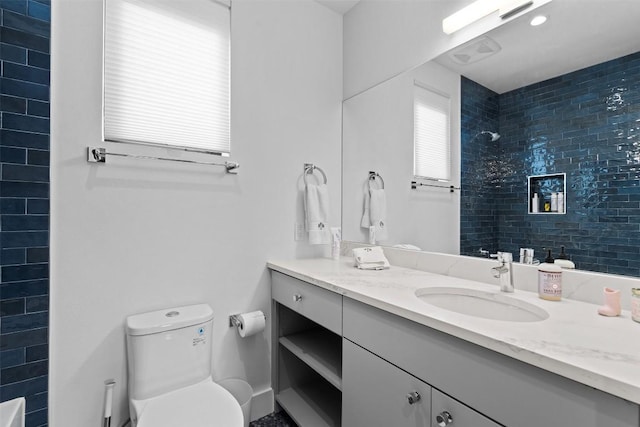 bathroom with a tile shower, toilet, and vanity