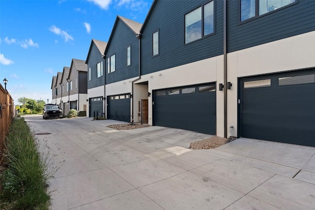 view of side of property featuring an attached garage, stucco siding, driveway, and a residential view