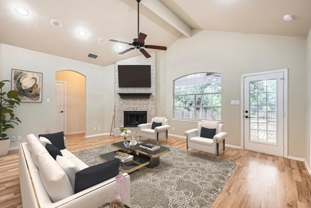 living room with a ceiling fan, arched walkways, a brick fireplace, light wood-style flooring, and baseboards