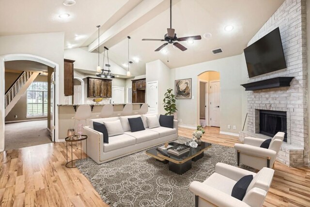 living area with arched walkways, light wood-style floors, a ceiling fan, a brick fireplace, and baseboards