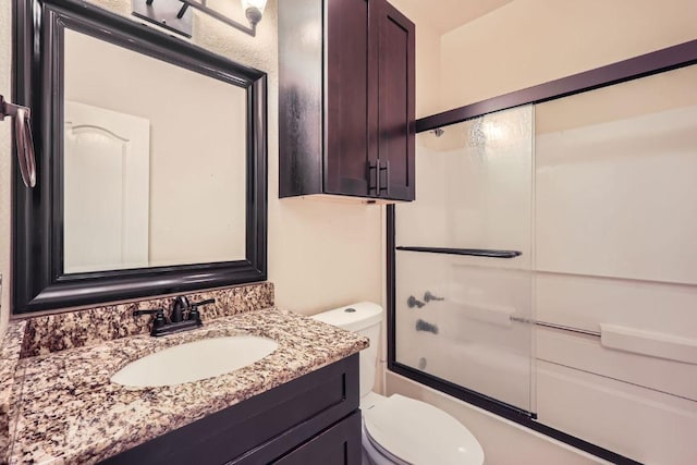 full bath with toilet, vanity, and shower / bath combination with glass door