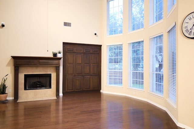 unfurnished living room with a towering ceiling, wood finished floors, baseboards, and a tile fireplace