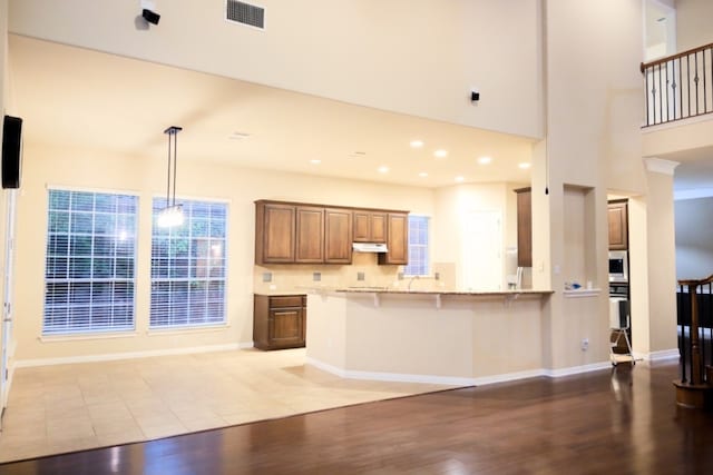 2702 Quiet Moon Trl, Cedar Park, TX 78613 - kitchen with under cabinet range hood, light wood finished floors, a kitchen bar, brown cabinets, and recessed lighting