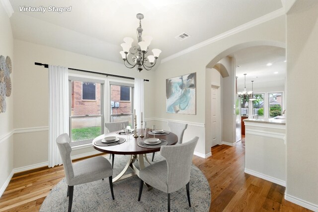dining space featuring a chandelier, arched walkways, light wood-type flooring, crown molding, and baseboards