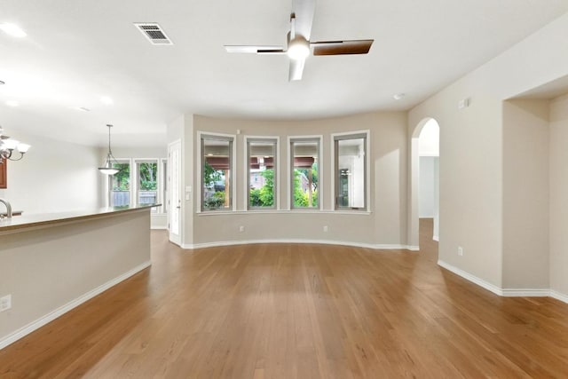 unfurnished living room with a ceiling fan, wood finished floors, arched walkways, and baseboards