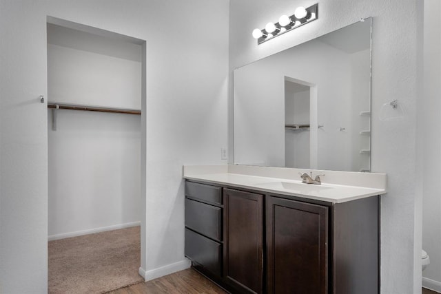 full bathroom with vanity, a spacious closet, toilet, and baseboards