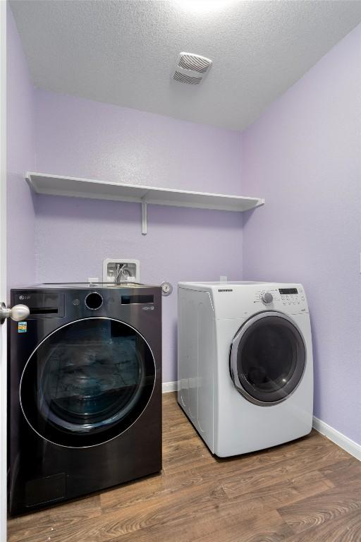 washroom featuring washing machine and clothes dryer, wood finished floors, baseboards, and a textured ceiling