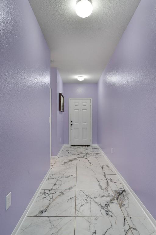 hall featuring baseboards, a textured ceiling, and light marble finish flooring