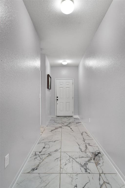 15013 Roody Ln, Austin, TX 78725 - hallway with baseboards, a textured ceiling, and light marble finish floors