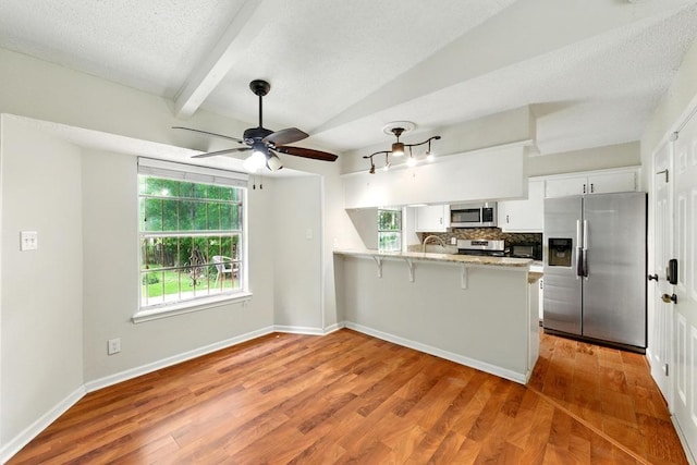 kitchen with appliances with stainless steel finishes, a peninsula, white cabinets, wood finished floors, and beamed ceiling