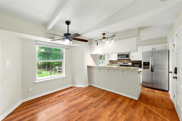 5103 Stone Gate Dr, Austin, TX 78721 - kitchen with appliances with stainless steel finishes, a peninsula, white cabinets, wood finished floors, and beamed ceiling
