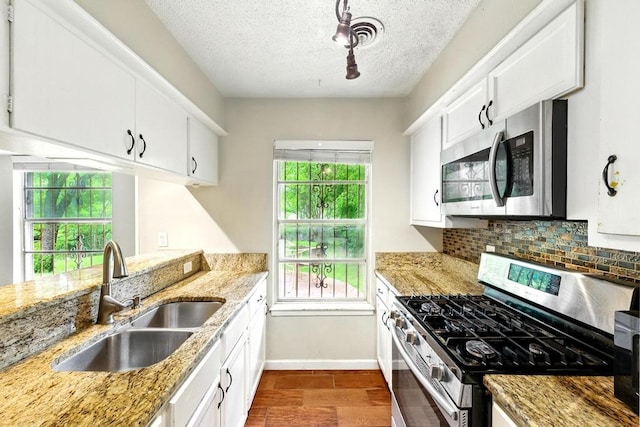 kitchen featuring stainless steel appliances, a sink, a textured ceiling, backsplash, and baseboards