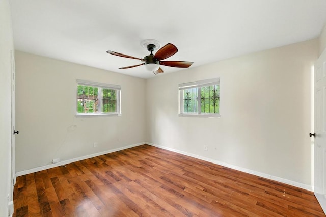 empty room with healthy amount of natural light, wood finished floors, a ceiling fan, and baseboards
