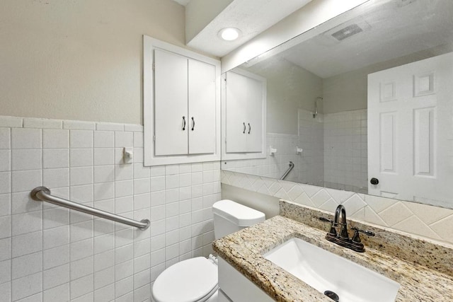 full bath with tile walls, a tile shower, toilet, and vanity