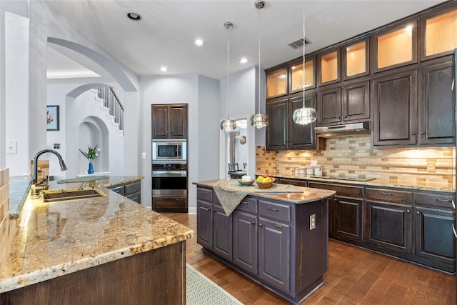 12013 Tarraza Ct, Austin, TX 78732 - kitchen featuring stainless steel appliances, a kitchen island, dark wood-type flooring, tasteful backsplash, and light stone countertops