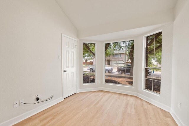 spare room featuring light wood-type flooring, baseboards, and lofted ceiling