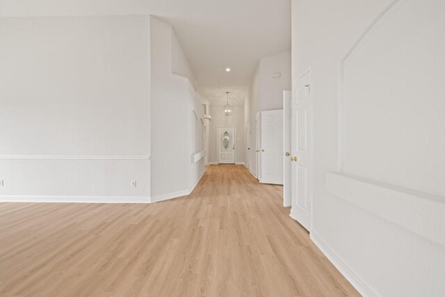 corridor featuring light wood-type flooring, baseboards, recessed lighting, and a chandelier